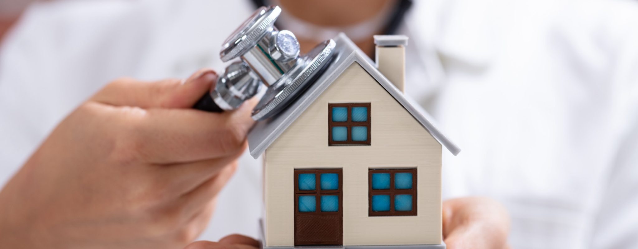 Close-up Of A Doctor's Hand Checking Simple Model House With Stethoscope